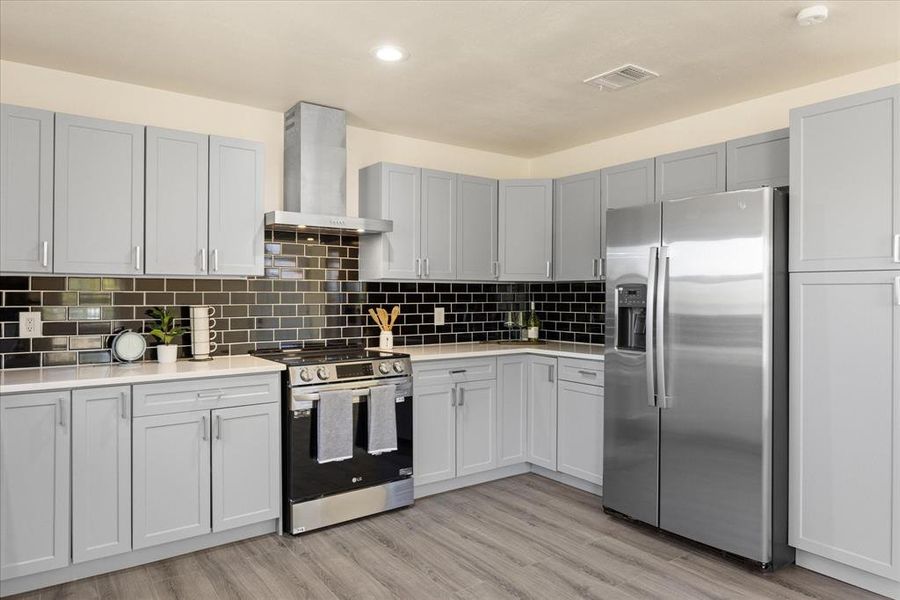 Kitchen with backsplash, light hardwood / wood-style flooring, wall chimney exhaust hood, and appliances with stainless steel finishes