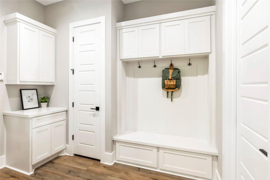 This photo showcases a bright, modern mudroom with white cabinetry, a built-in bench, and storage hooks This photo showcases a bright, modern mudroom with white cabinetry, a built-in bench, and storage hooks