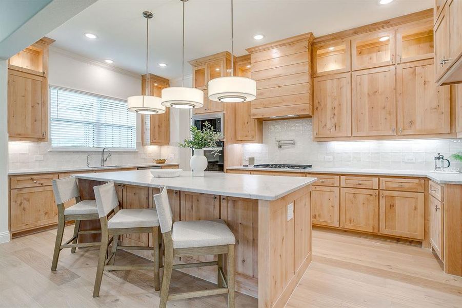 Kitchen with custom Knotty Alder wood cabinets to the ceiling, leathered Quartzite counters, tile backsplash, decorative lighting, ample storage, soft close doors and drawers, and gas cooktop.