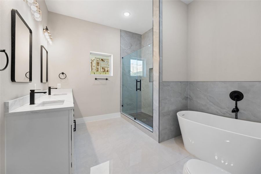 This modern bathroom features a sleek double vanity with black fixtures, a spacious glass-enclosed shower, and a freestanding bathtub. The neutral color palette adds a touch of elegance.