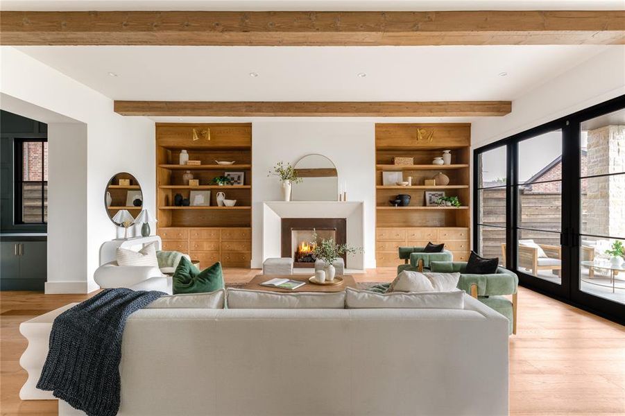 Living room featuring built in shelves, light wood finished floors, beam ceiling, and a lit fireplace