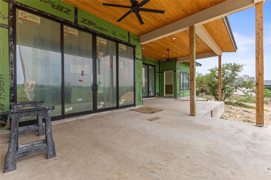 Spacious outdoor patio featuring a concrete surface, exposed wood ceiling with integrated fans, and expansive sliding glass doors