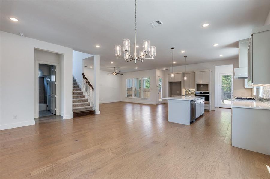 Kitchen featuring white cabinetry, hanging light fixtures, ceiling fan with notable chandelier, an island with sink, and light hardwood / wood-style flooring