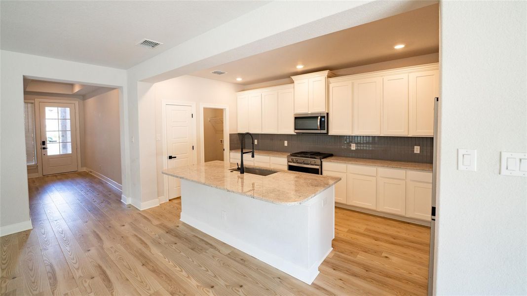 Kitchen with tasteful backsplash, appliances with stainless steel finishes, light stone counters, white cabinets, and recessed lighting Kitchen with tasteful backsplash, appliances with stainless steel finishes, light stone counters, white cabinets, and recessed lighting