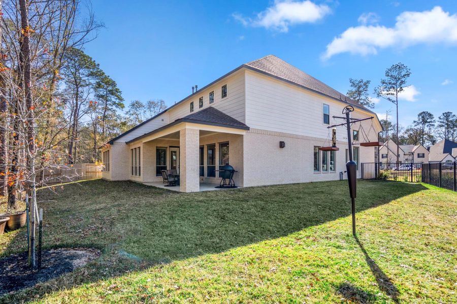 Enjoy a spacious backyard with a covered patio area perfect for outdoor dining. The property is bordered by trees, providing a sense of privacy and a connection to nature.