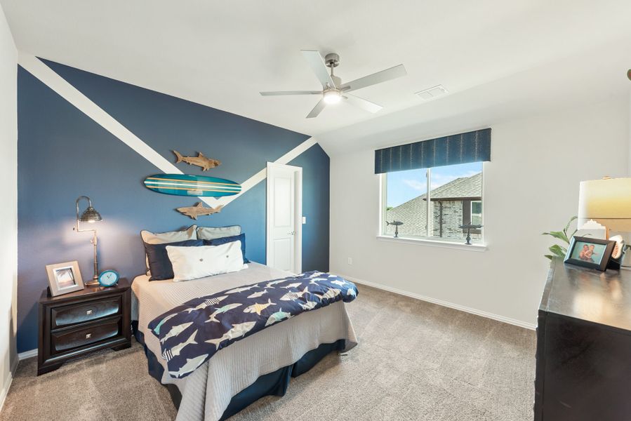 Children's bedroom with navy blue accent wall, surfboard decor, ceiling fan, and carpeted floors