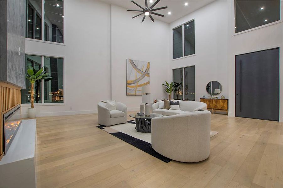 Living room with ceiling fan, a high ceiling, and light wood-type flooring