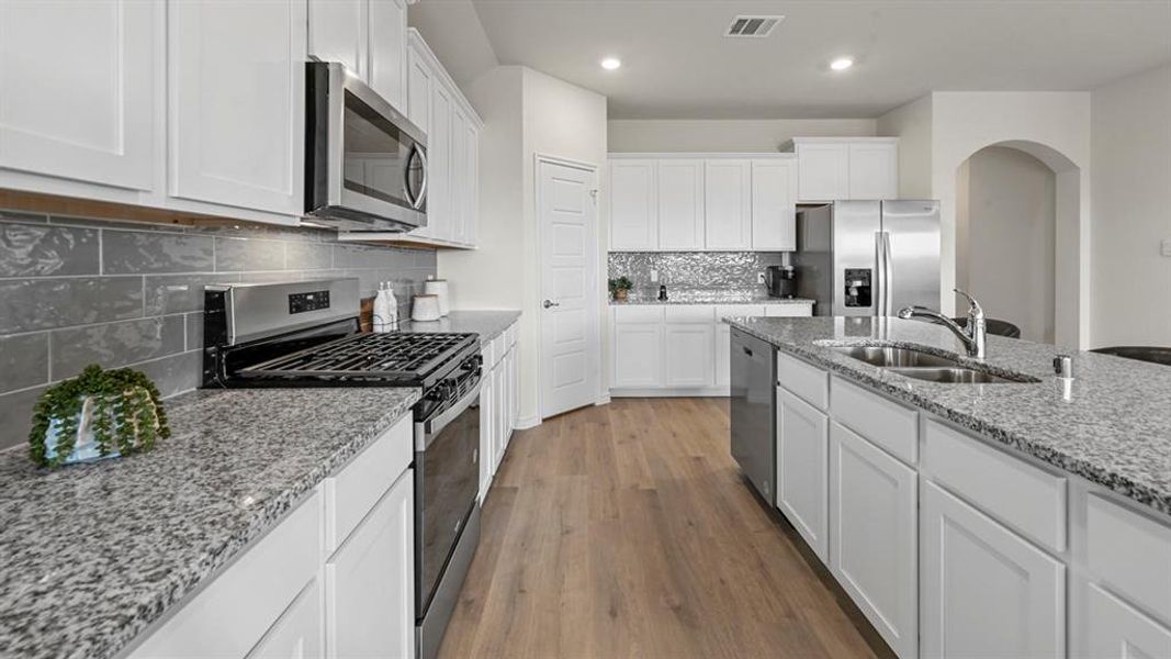 Kitchen featuring stainless steel appliances, white cabinets, dark wood-style floors, light stone countertops, and decorative backsplash