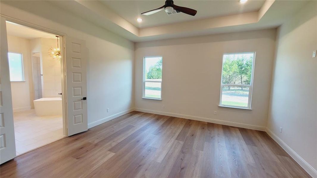 Spacious room featuring wood-finish flooring, a tray ceiling with recessed lighting, and a ceiling fan
