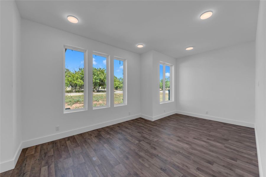 Entry flex/office space at front of home.  Rich wood-look flooring and recessed lighting complement large windows framing peaceful green views.