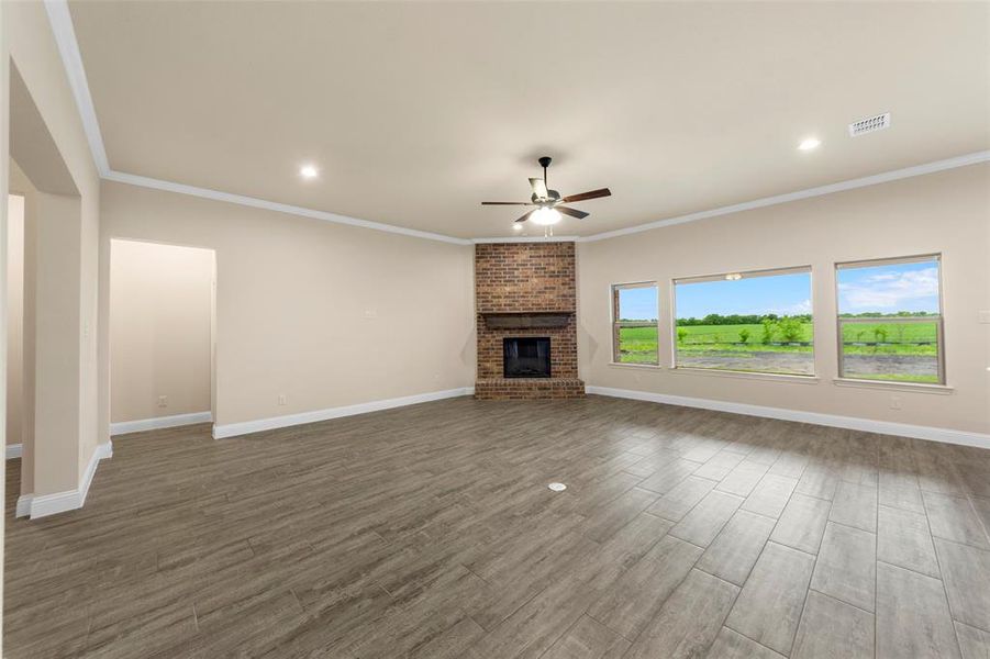 Unfurnished living room featuring a ceiling fan, wood finished floors, a brick fireplace, crown molding, and baseboards