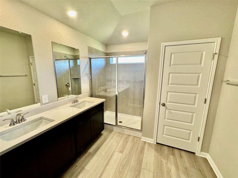 Full bathroom featuring vaulted ceiling, a stall shower, wood finished floors, and double vanity Full bathroom featuring vaulted ceiling, a stall shower, wood finished floors, and double vanity