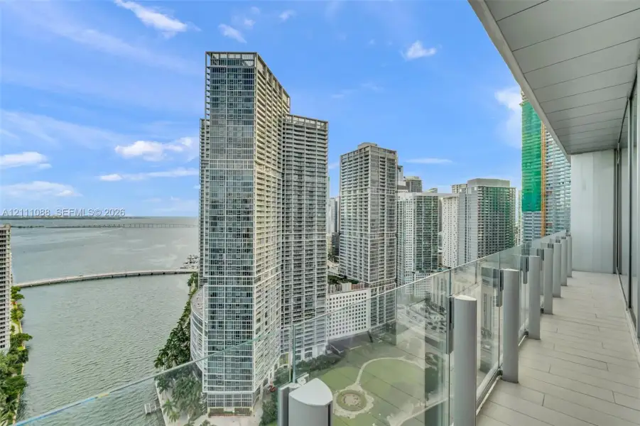 Covered outdoor balcony featuring light-toned tile flooring and transparent glass panel railings Covered outdoor balcony featuring light-toned tile flooring and transparent glass panel railings