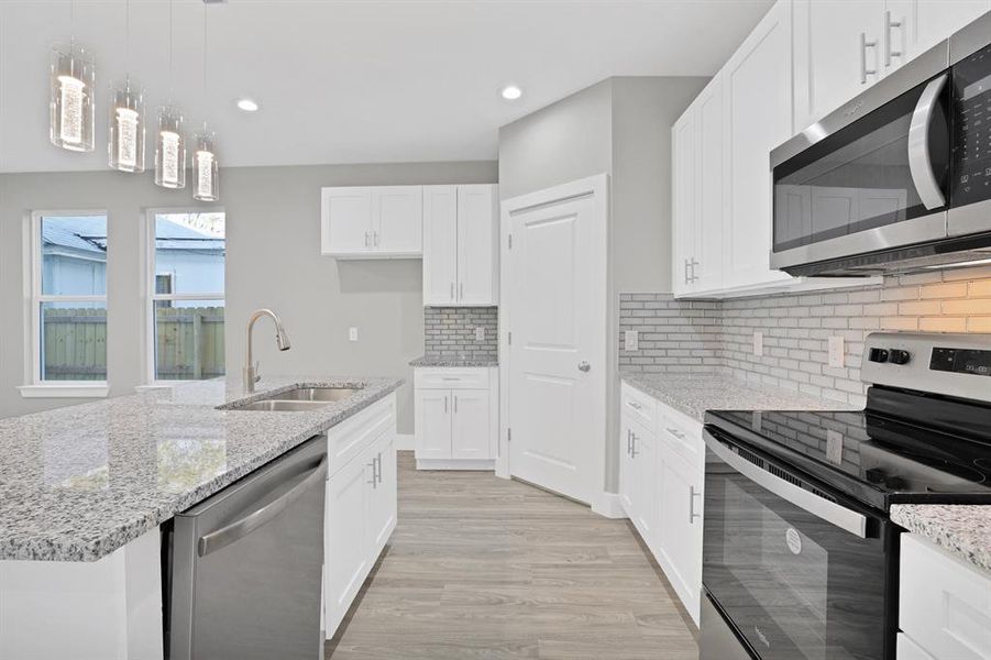 Kitchen featuring appliances with stainless steel finishes, light wood-type flooring, sink, a center island with sink, and white cabinets