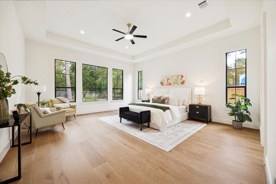 Spacious primary bedroom with tray ceiling, white oak wood floors, and large windows offering great natural light.