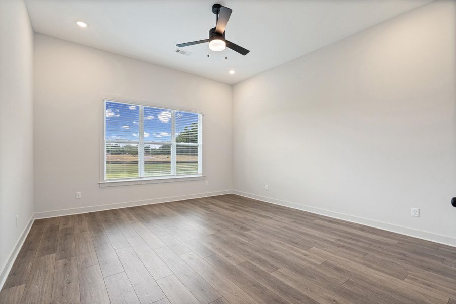 Spacious room featuring wood-finish flooring, a large window with blinds, recessed lighting, a ceiling fan, and white baseboards Spacious room featuring wood-finish flooring, a large window with blinds, recessed lighting, a ceiling fan, and white baseboards
