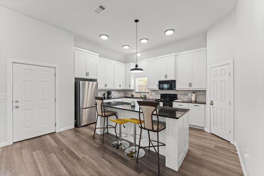 Kitchen featuring white cabinetry, hanging light fixtures, a center island, and black appliances
