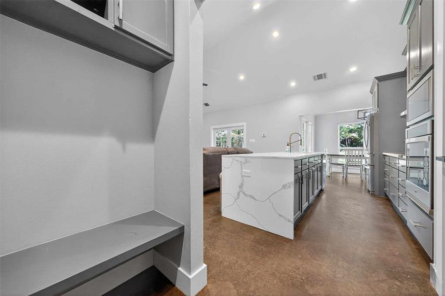Kitchen with recessed lighting, a center island with sink, light stone counters, concrete flooring, and open floor plan Kitchen with recessed lighting, a center island with sink, light stone counters, concrete flooring, and open floor plan