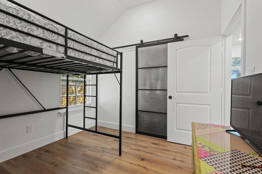 Unfurnished bedroom featuring a barn door, light wood finished floors, and vaulted ceiling