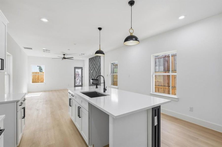 Kitchen featuring white cabinetry, light wood-type flooring, recessed lighting, a center island with sink, and hanging light fixtures Kitchen featuring white cabinetry, light wood-type flooring, recessed lighting, a center island with sink, and hanging light fixtures