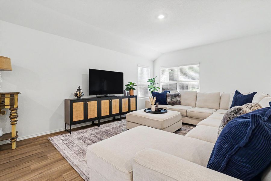 Spacious living area featuring wood-finish flooring, vaulted ceilings, and recessed lighting