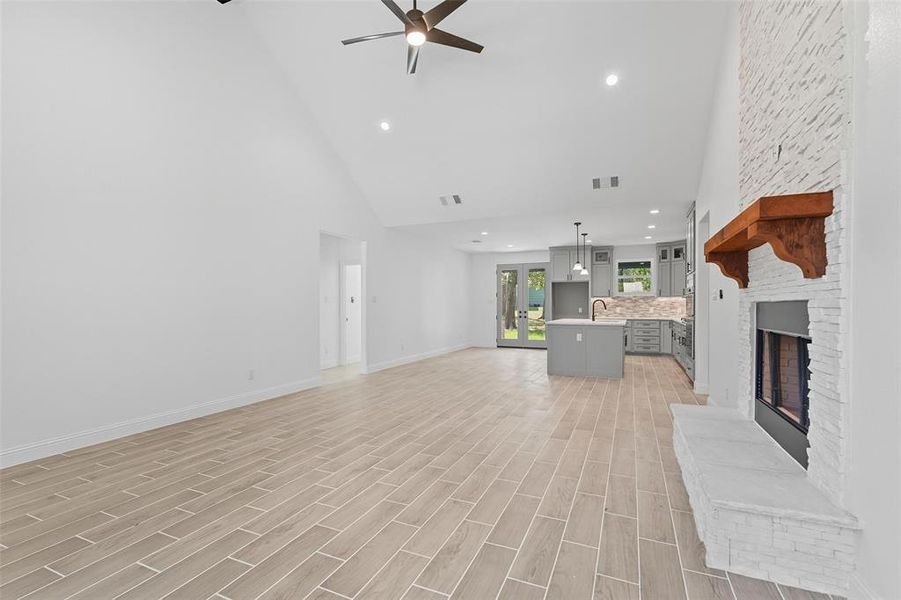 Unfurnished living room featuring high vaulted ceiling, a fireplace, french doors, wood tiled floors, and recessed lighting Unfurnished living room featuring high vaulted ceiling, a fireplace, french doors, wood tiled floors, and recessed lighting