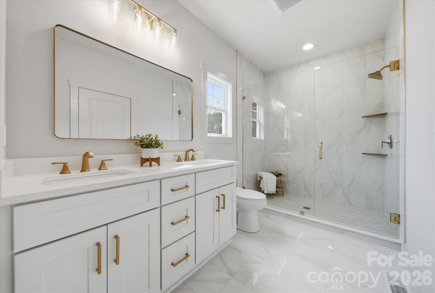 Primary bathroom with double vanity, floor to ceiling tiled shower, gold hardware finishes