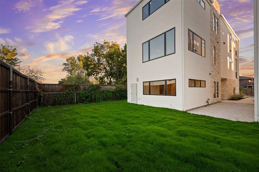 Back of house with stucco siding, a fenced backyard, and stone siding