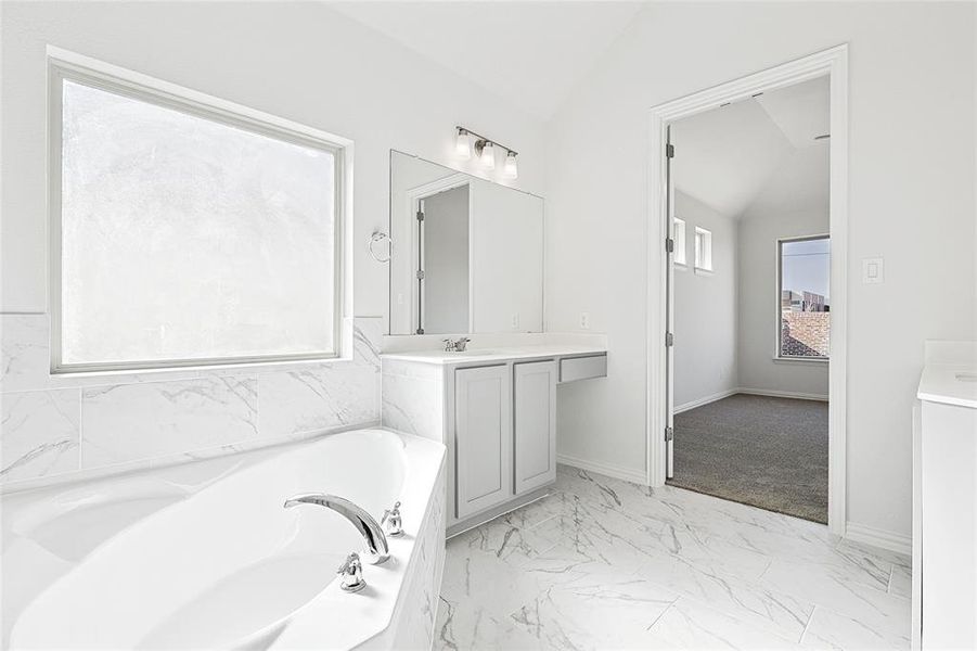 Full bathroom featuring light marble finish floors, vanity, vaulted ceiling, and a bath Full bathroom featuring light marble finish floors, vanity, vaulted ceiling, and a bath