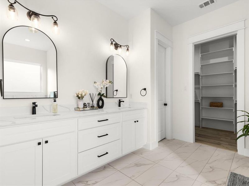 Bathroom featuring double vanity, light marble finish floors, and a spacious closet