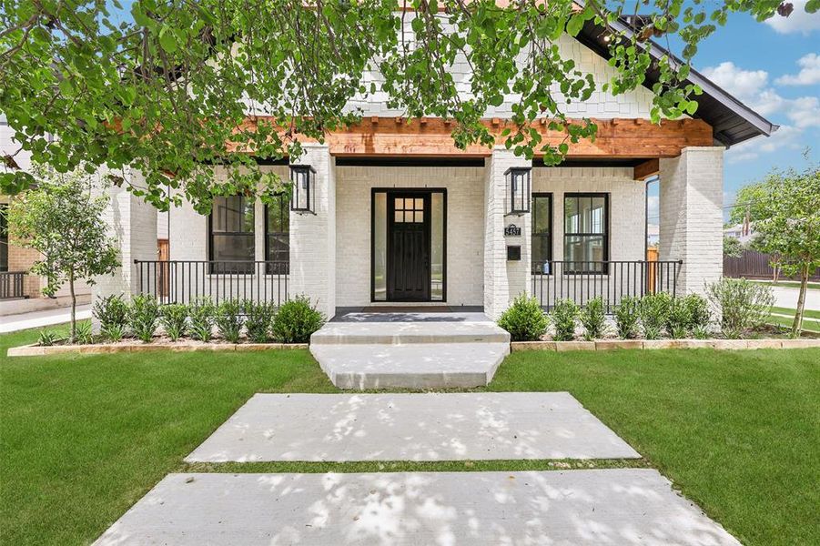 Contemporary white brick exterior with dark trim accents, featuring a covered porch with black railings, wood-beam details, and a concrete pathway