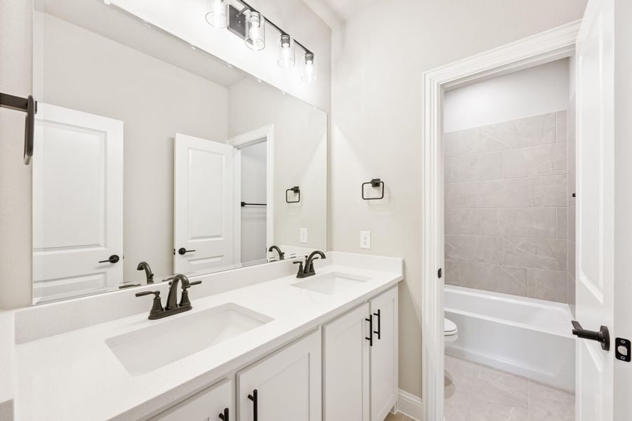 Bathroom with double sink vanity, white cabinets, large mirror, and tiled tub-shower combo visible through doorway