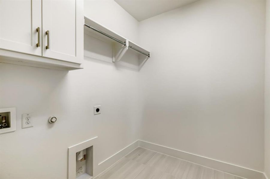 Bright utility space featuring white upper cabinetry with bronze hardware, a built-in hanging rod, and light wood-finish flooring