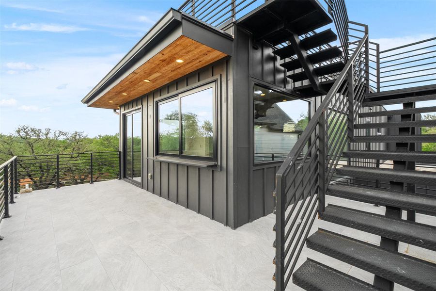 Expansive outdoor terrace featuring light-colored tiling, dark metal railings, and a stairway with metal steps