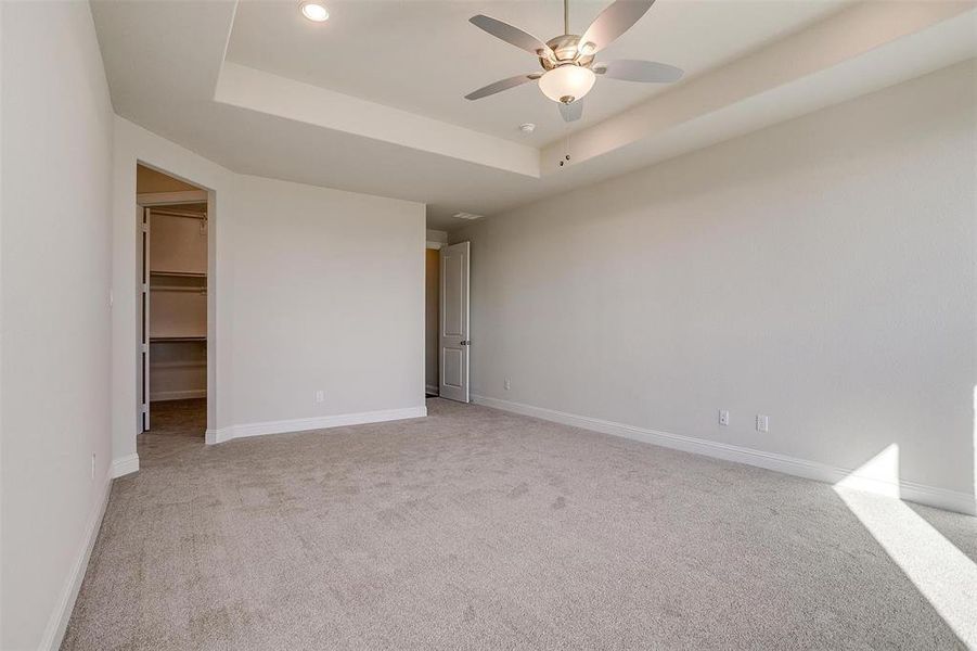 Carpeted empty room featuring ceiling fan and a raised ceiling