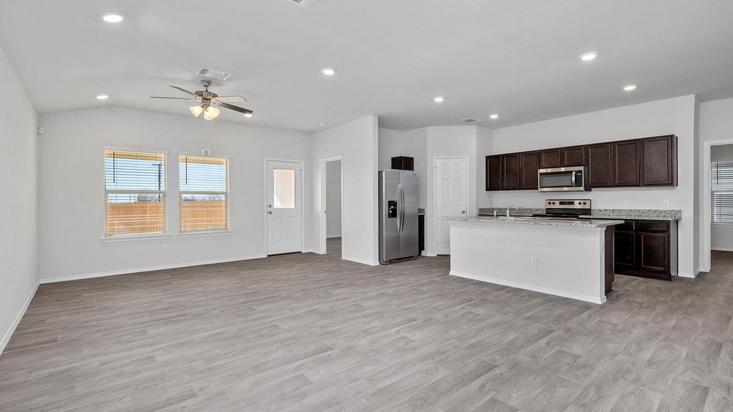 Kitchen with open floor plan, dark wood finish cabinetry, stainless steel appliances, recessed lighting, and an island with sink