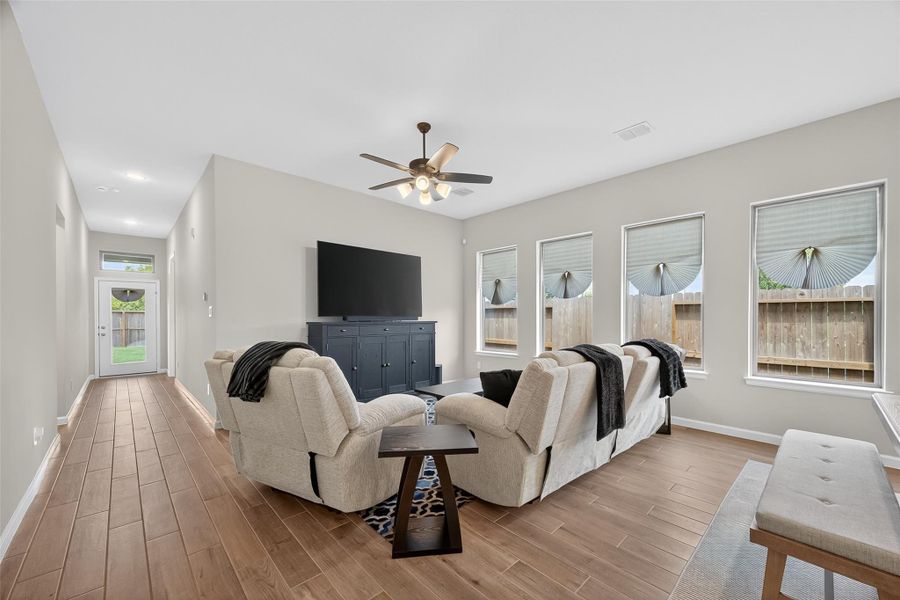 This living room features a spacious layout with wood-look flooring, ample natural light from multiple windows, and a ceiling fan. It includes comfortable seating. This living room features a spacious layout with wood-look flooring, ample natural light from multiple windows, and a ceiling fan. It includes comfortable seating.