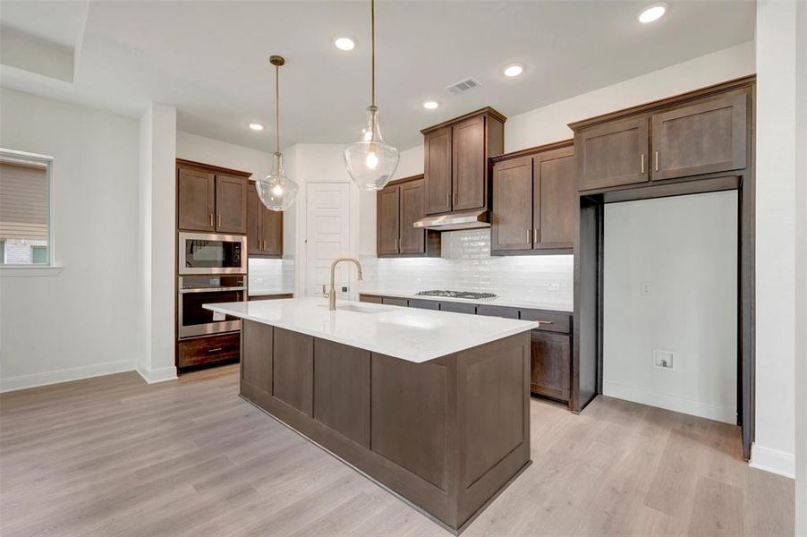 Modern kitchen featuring dark wood cabinetry, white subway tile backsplash, and light wood-finish flooring