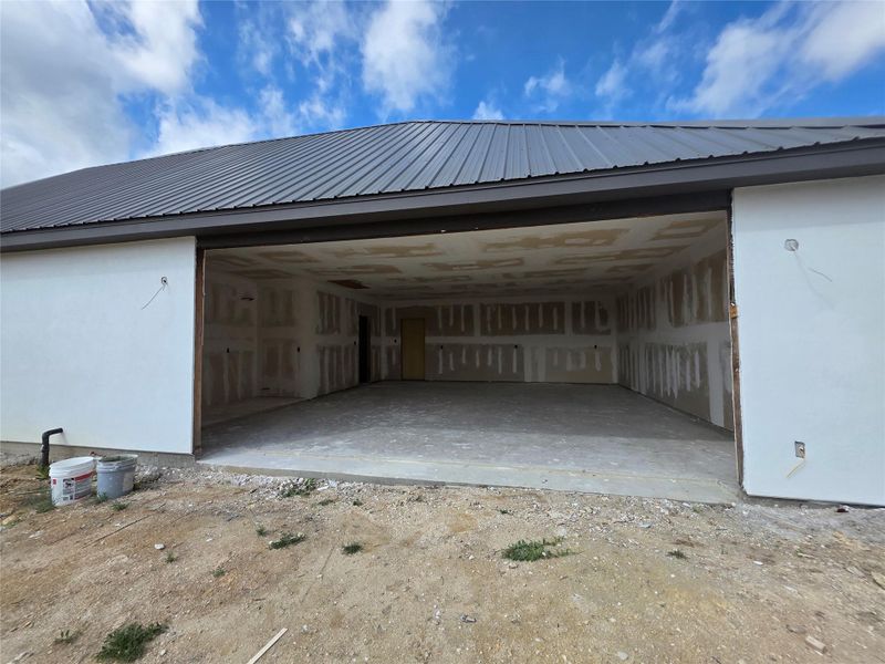 Spacious multi-car garage space under construction, featuring a concrete slab floor, unfinished drywall, and an exposed ceiling