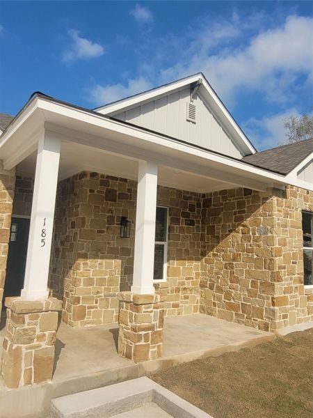 Property entrance featuring a porch, stone siding, and a shingled roof