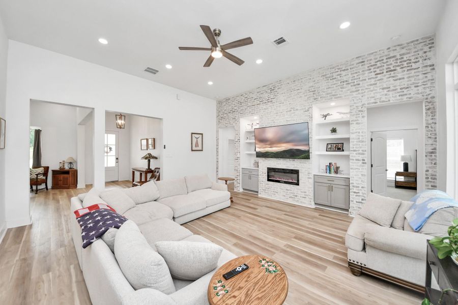 Spacious living room with a stylish brick accent wall, and a modern built-in entertainment center featuring a sleek fireplace and ample shelving. Spacious living room with a stylish brick accent wall, and a modern built-in entertainment center featuring a sleek fireplace and ample shelving.