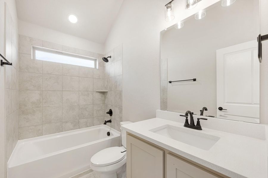 Bathroom with tiled tub-shower combo, white vanity with quartz countertop, and black fixtures