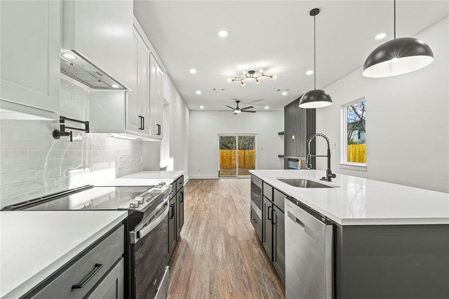 Kitchen featuring stainless steel appliances, light stone countertops, decorative light fixtures, dark wood-style flooring, and open floor plan