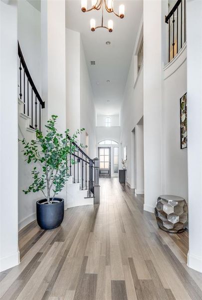 Entryway featuring stairs, a towering ceiling, light wood-style flooring, and a chandelier