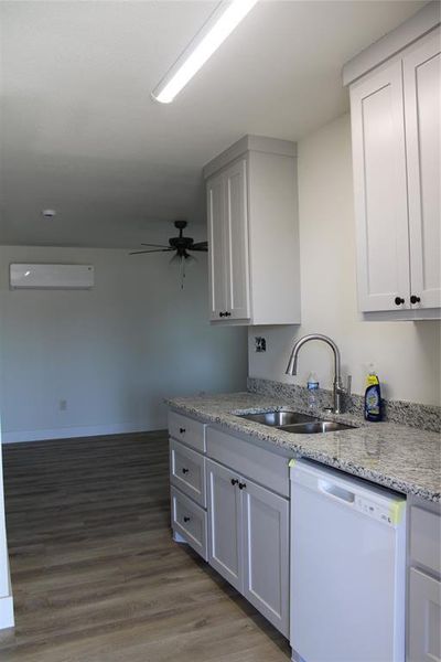Kitchen with dishwasher, light stone countertops, white cabinetry, and light wood-style flooring
