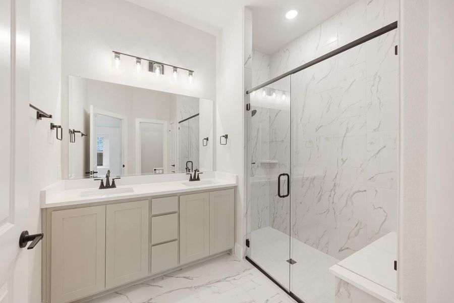 Bathroom with double vanity, large mirror, and glass-enclosed shower with marble tile walls and floors