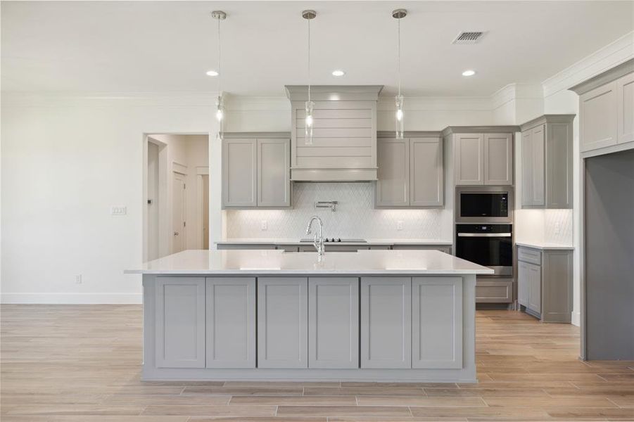 Kitchen featuring a kitchen island with sink, stainless steel appliances, tasteful backsplash, and gray cabinetry