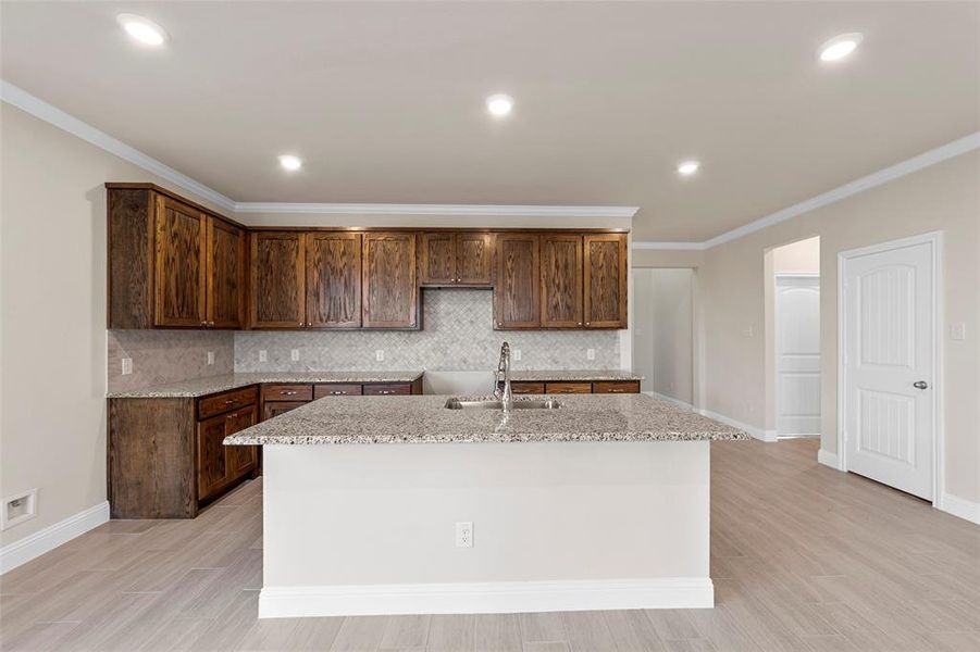 Kitchen with light stone countertops, sink, tasteful backsplash, an island with sink, and ornamental molding