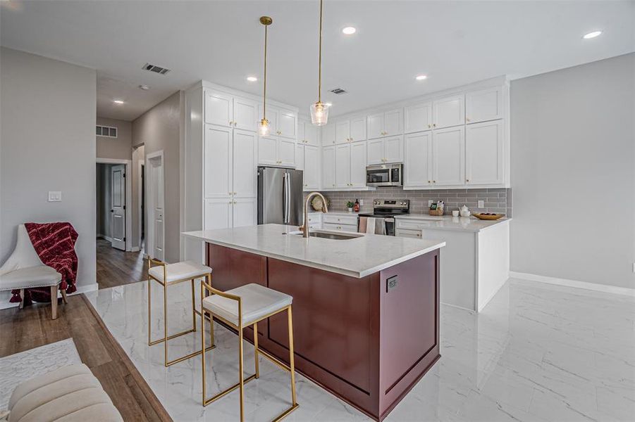 Kitchen with stainless steel appliances, an island with sink, light stone countertops, a kitchen bar, and tasteful backsplash