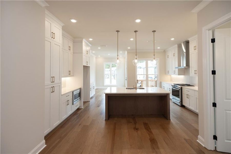 Kitchen featuring appliances with stainless steel finishes, a kitchen island with sink, wall chimney range hood, and white cabinets